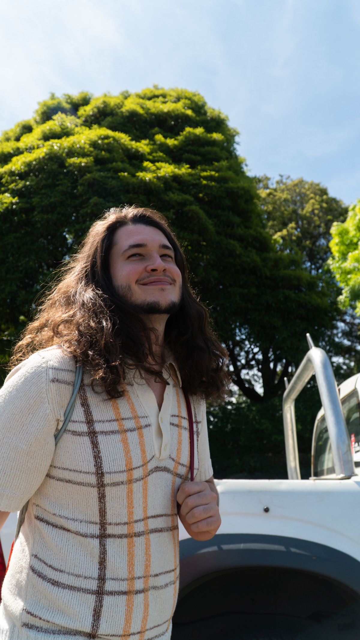 Jean-Luc Alder, smiling in the sun in front of a white car and a large green tree